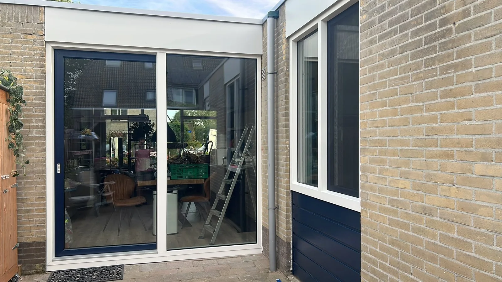Nieuwe schuifpui met blauwe en witte kozijnen aan een tuin